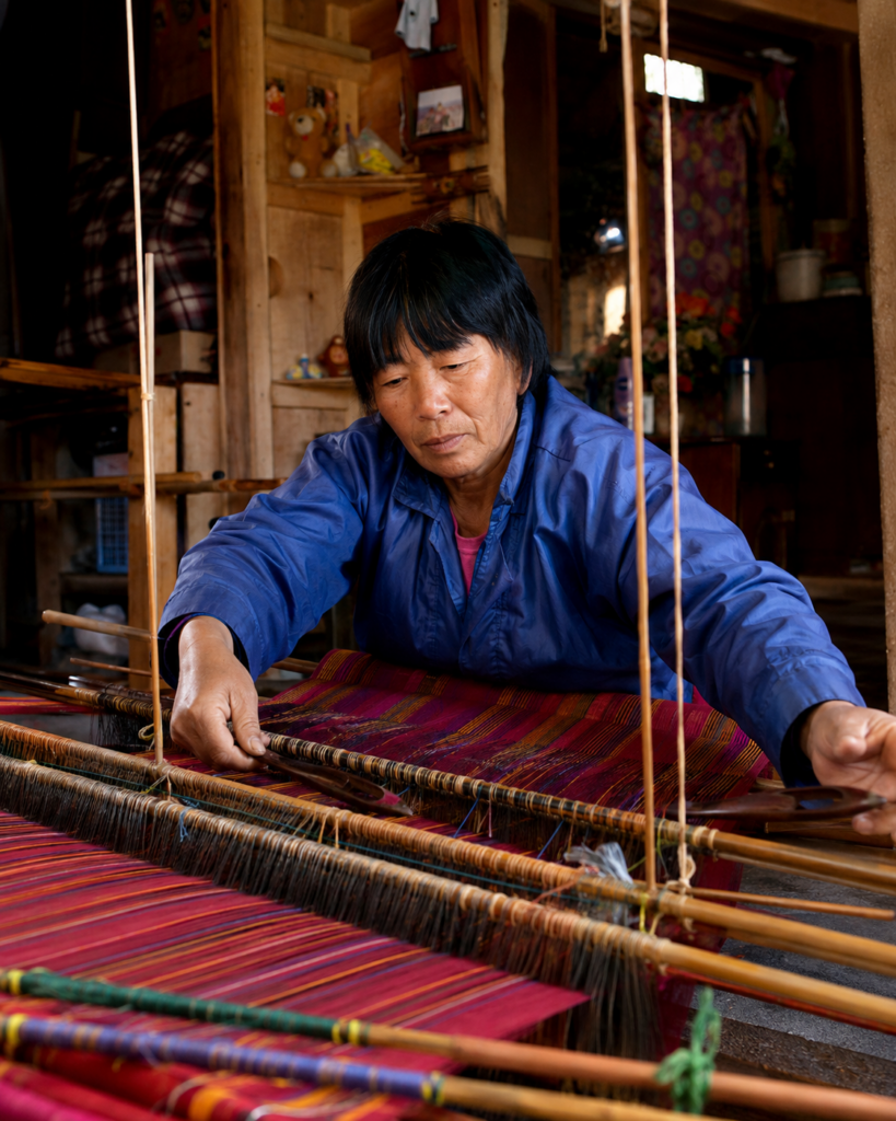 Bhutanese woman weaving colourful traditional fabric on a loom in a home workshop.